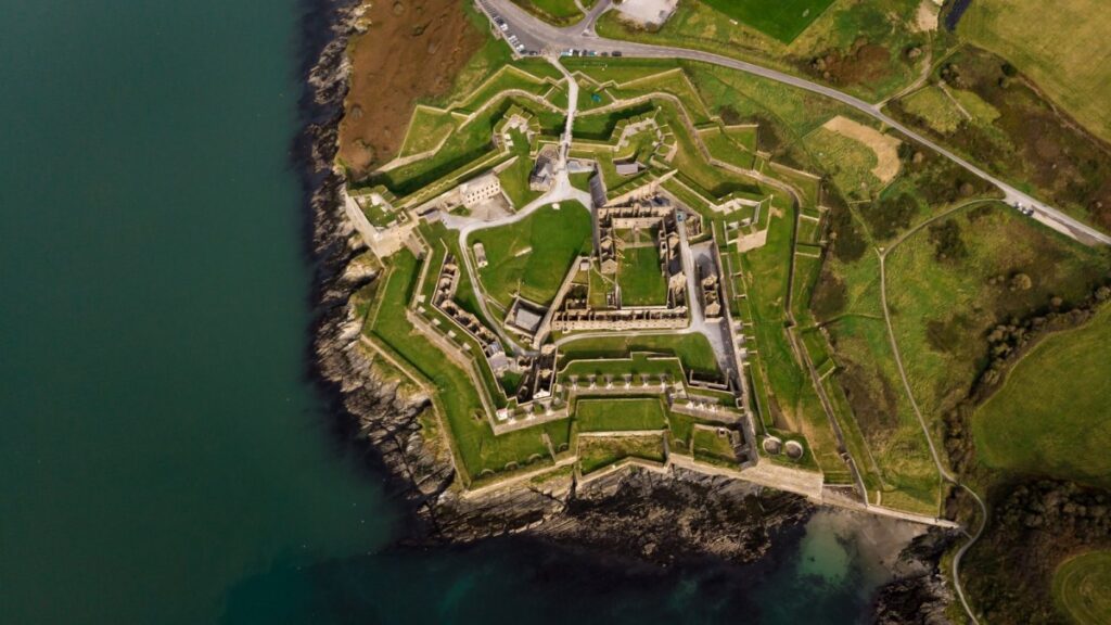 Aerial view of star-shaped coastal fortress with defensive walls and green grounds beside turquoise water