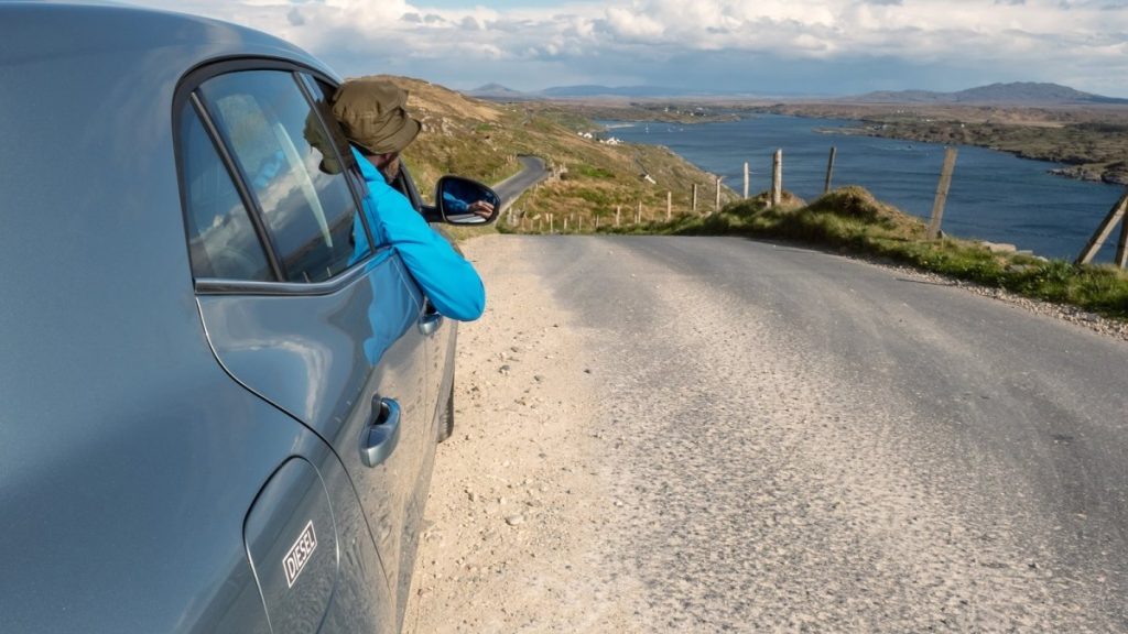 Blue van parked on gravel coastal road overlooking Irish bay and mountains