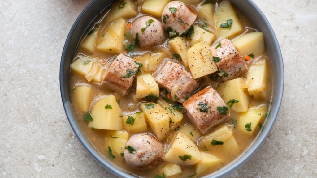 Bowl of Irish stew with sausages, potatoes, and fresh parsley garnish