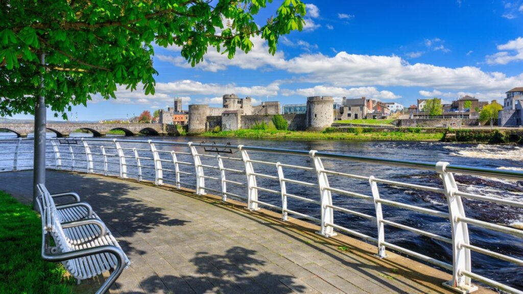 Waterfront promenade with white railings overlooking river and medieval castle ruins