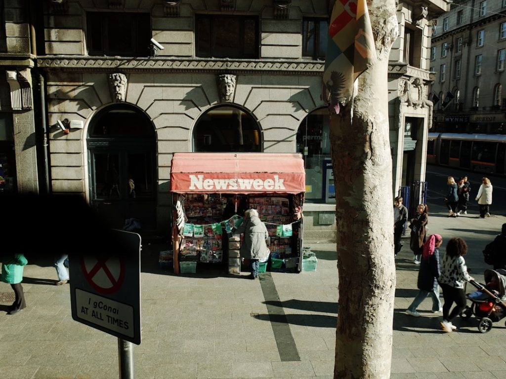 A newsweek kiosk on a bustling city street with people