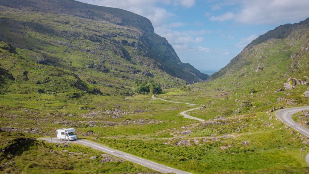White motorhome parked on winding road through green mountain valley