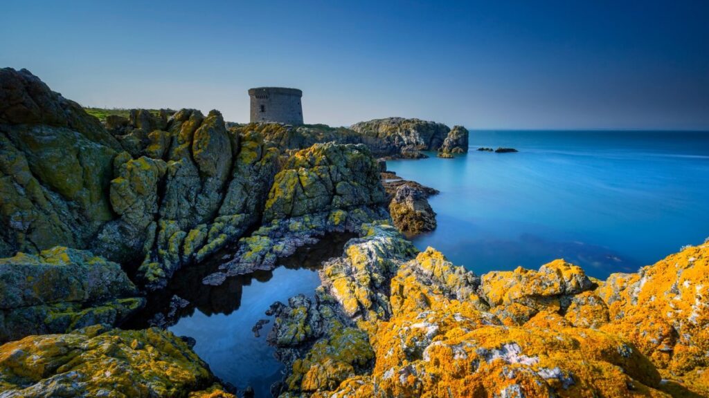 Coastal tower ruins perched on rocky headland overlooking bright blue sea