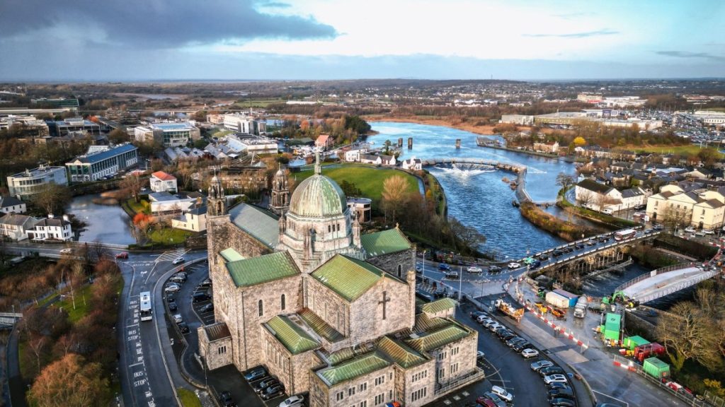 Aerial view of a cathedral with copper dome overlooking a river and sprawling cityscape